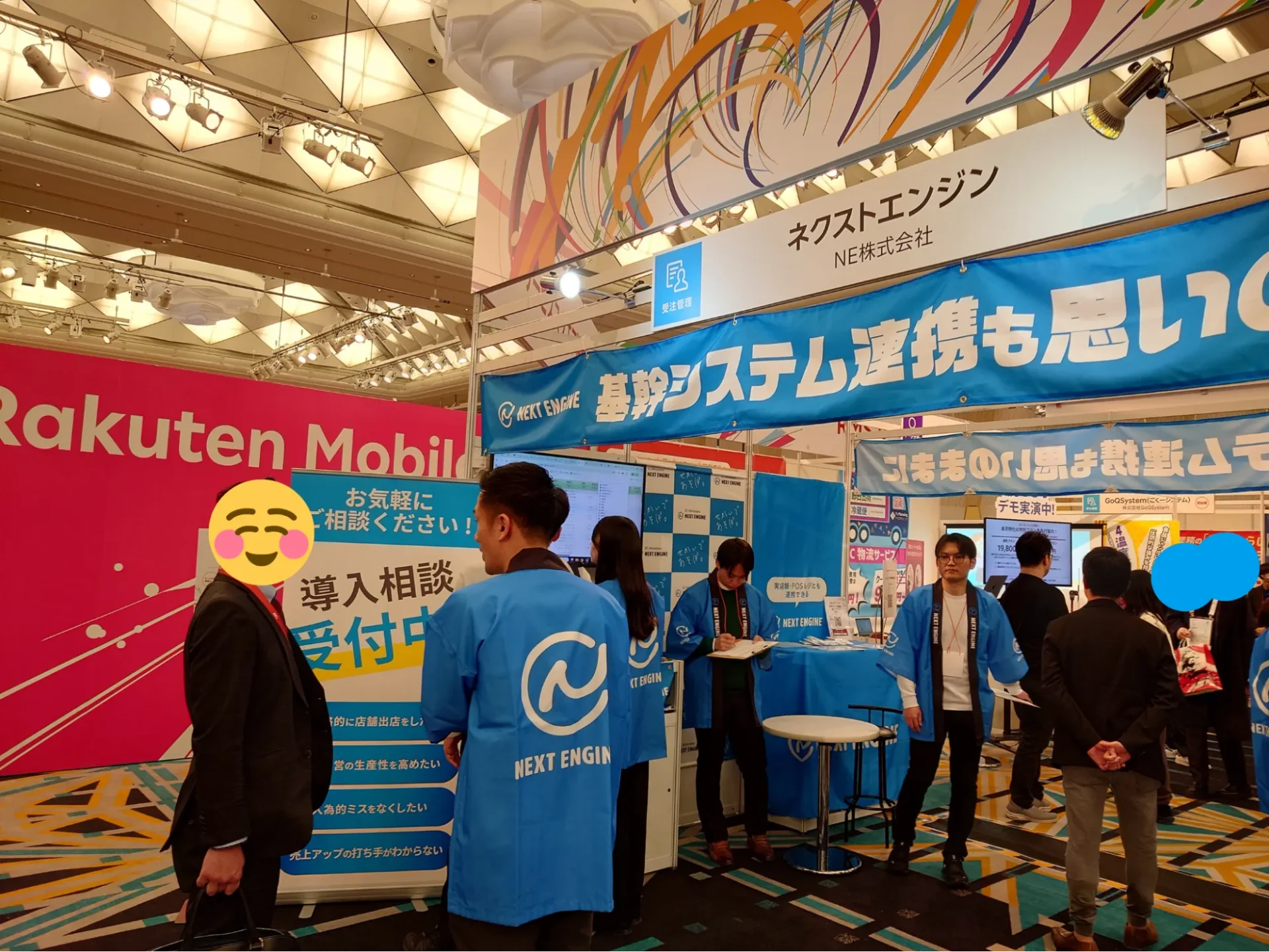 楽天新春カンファレンスの「導入相談受付中」パネルが置かれたネクストエンジンブース前で、スタッフが来場者の相談に応じている様子。
