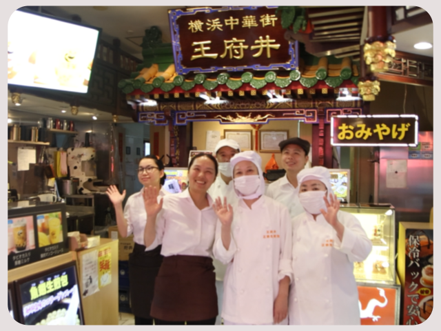 活気あふれるお店の入り口で、調理スタッフやホール担当の従業員が、チーム一丸となってお客様を歓迎している様子。温かいおもてなしの気持ちが伝わってきます。